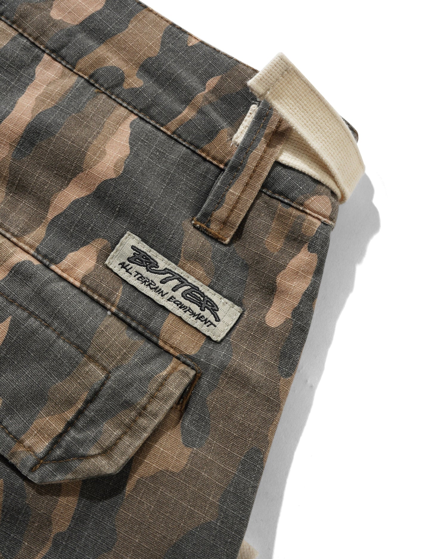 Close-up of camouflage pants showing a front flap pocket, belt loop, waistband, and a sewn-on brand patch that reads RITTER All Terrain Apparel.