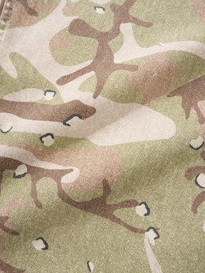 A close-up of camouflage-patterned fabric with irregular patches of muted olive green, tan, beige, and brown, plus a few small dark accents.