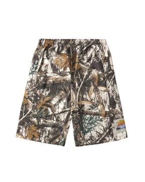A pair of camouflage shorts with an all-over woodland tree branch and leaf pattern in brown, beige, and green tones, featuring an elastic waistband and a small brand patch on the lower left leg.