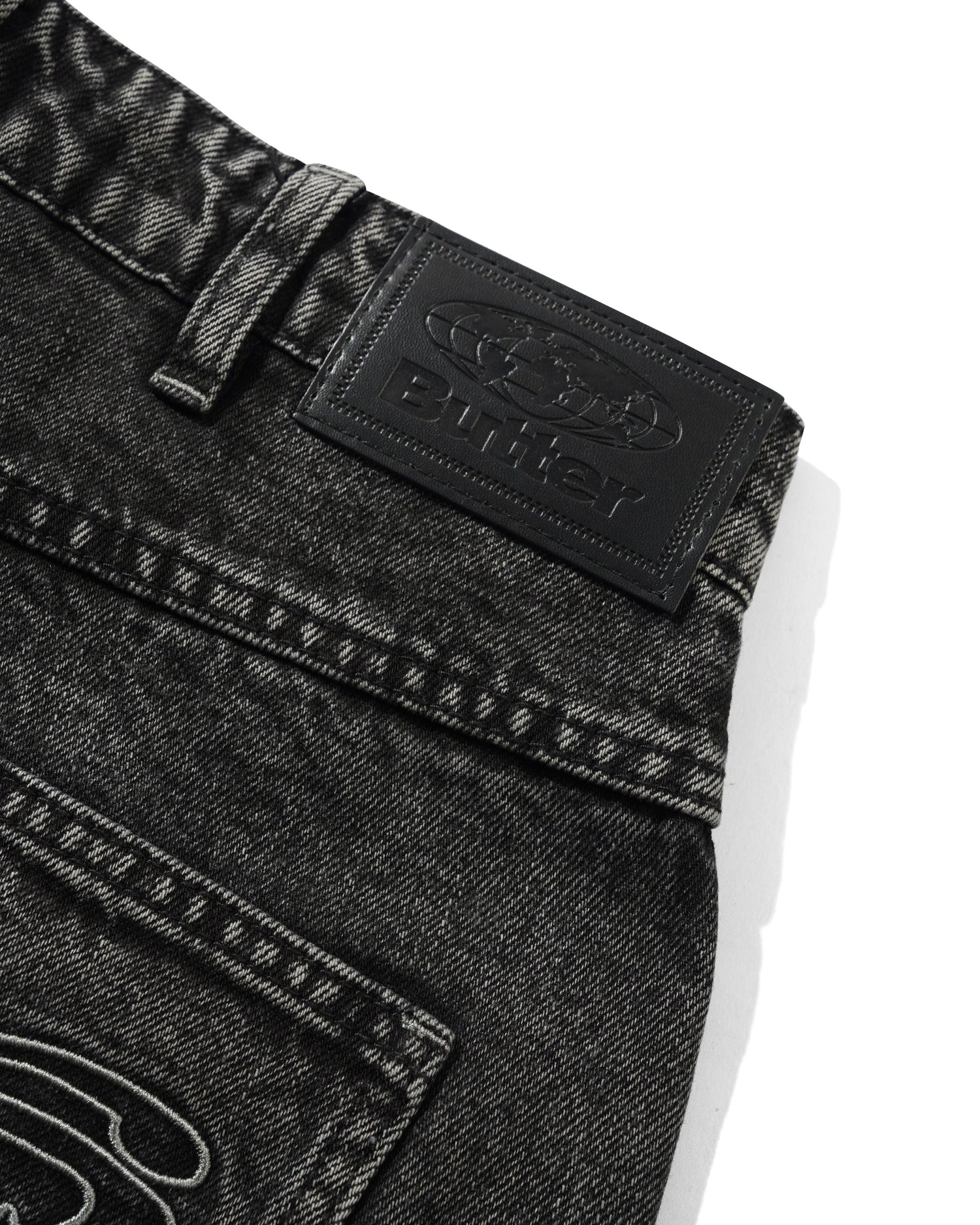 Close-up of black denim jeans with a brand logo on a white background