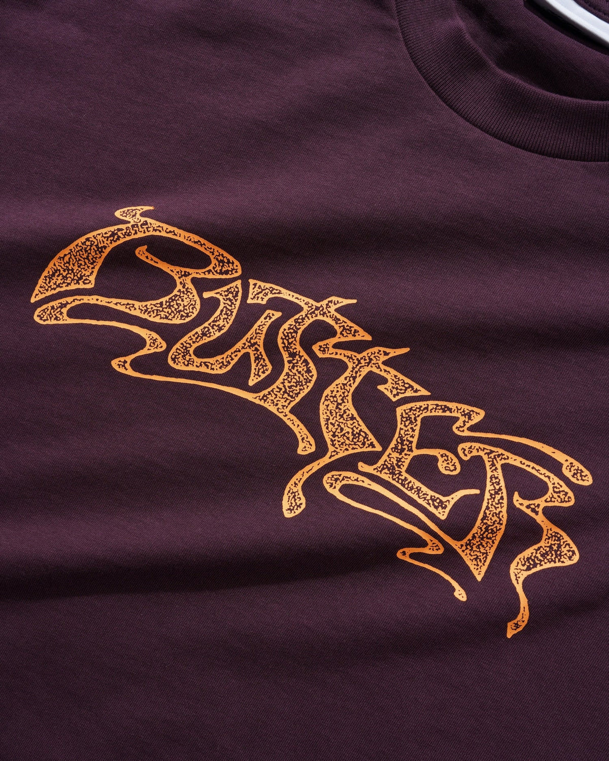Gold embroidered logo on a maroon fabric background