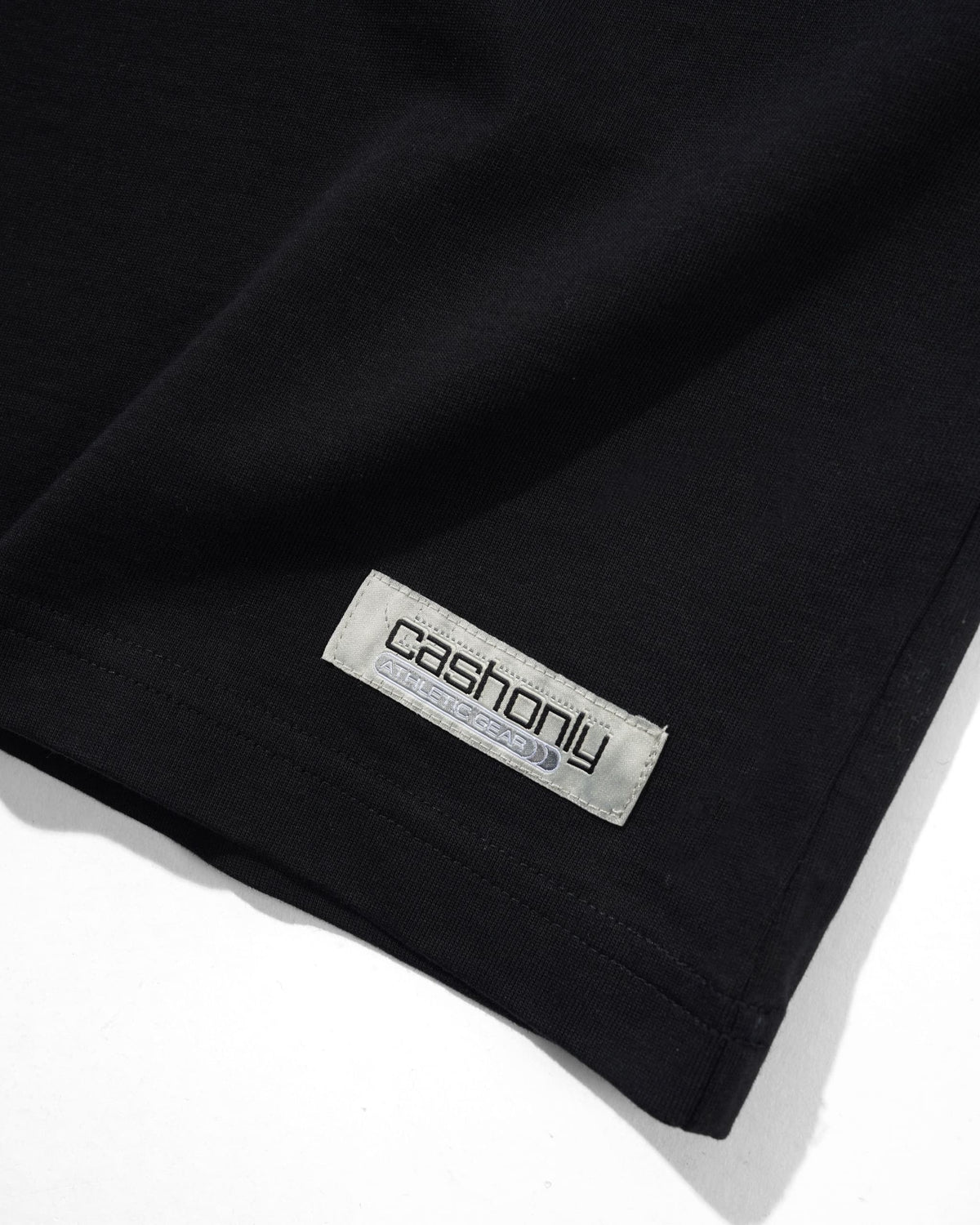 Close-up of a black garment corner with a visible rectangular brand label reading 'cashonly' on a white background.