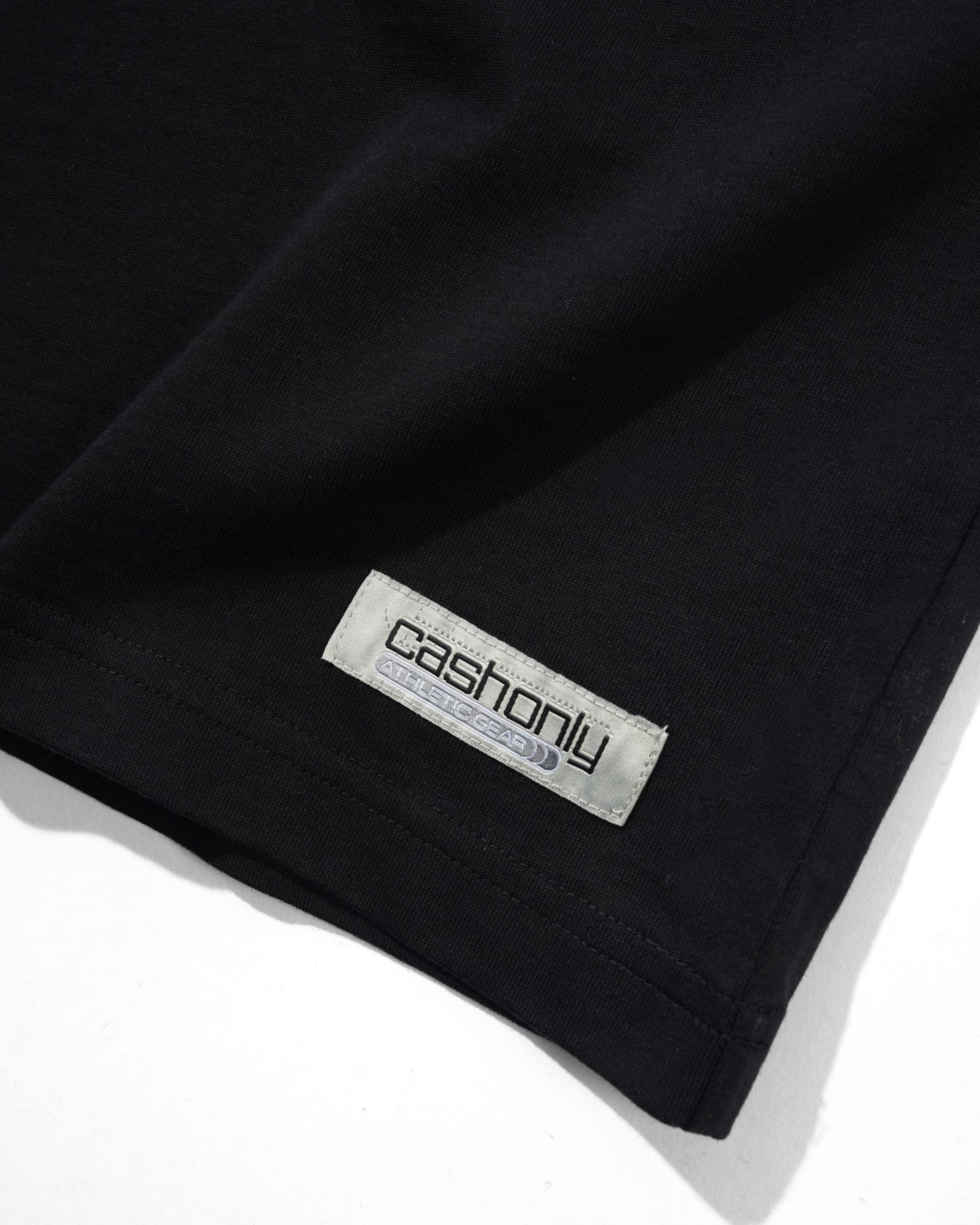 Close-up of a black garment corner with a visible rectangular brand label reading 'cashonly' on a white background.