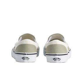 Pair of white slip-on sneakers with gray soles on a light beige background