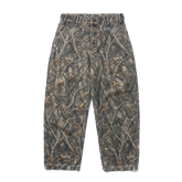 A pair of camouflage pants with a realistic woodland tree branch and leaf pattern in shades of gray, brown, and beige, shown flat against a solid white background.