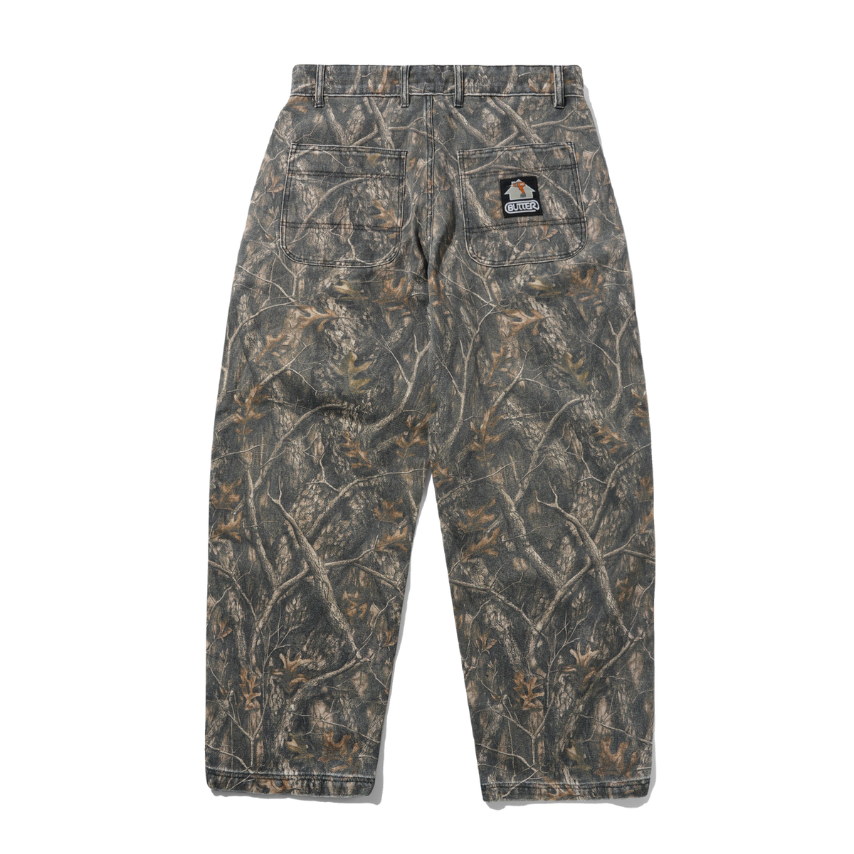 A pair of camouflage pants shown from the back, featuring a realistic woodland branch and leaf pattern in shades of brown, gray, and beige. A small embroidered patch is visible on the upper right back pocket.
