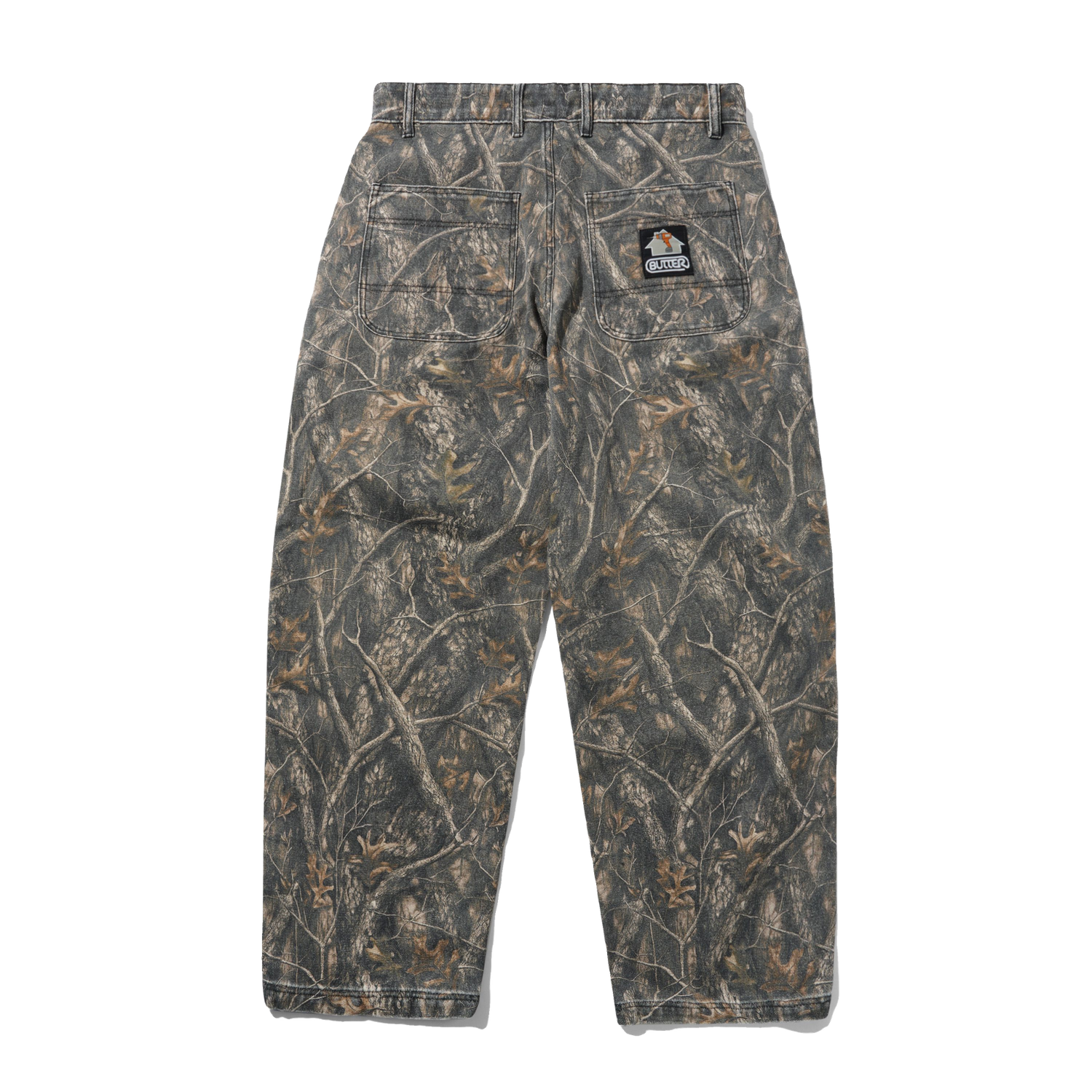 A pair of camouflage pants shown from the back, featuring a realistic woodland branch and leaf pattern in shades of brown, gray, and beige. A small embroidered patch is visible on the upper right back pocket.