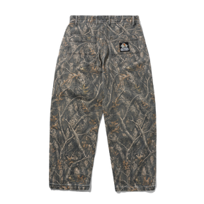A pair of camouflage pants shown from the back, featuring a realistic woodland branch and leaf pattern in shades of brown, gray, and beige. A small embroidered patch is visible on the upper right back pocket.